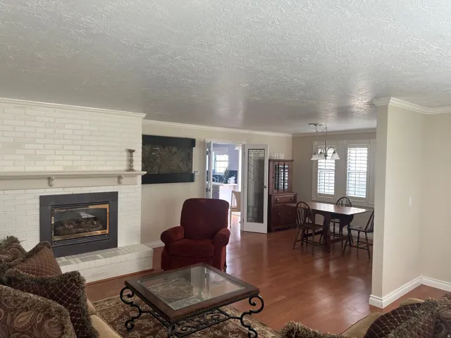 Brick-surround fireplace with a mantel, wood-finish flooring, and crown molding throughout