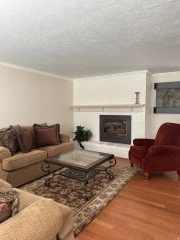 White painted brick fireplace with hearth, wood-finish flooring, and crown molding