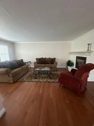 Expansive room featuring rich wood-finish flooring, a white brick fireplace with a mantel, and crown molding