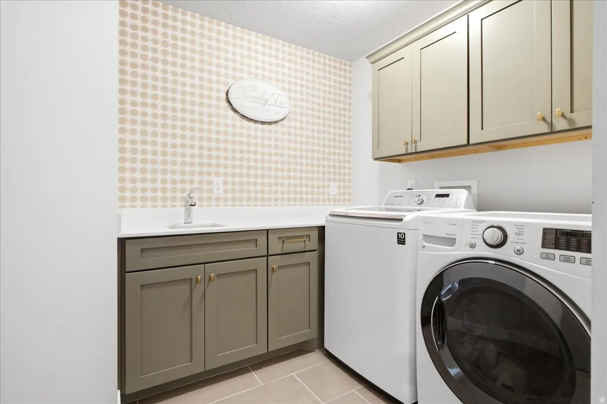 Dedicated laundry room featuring a washer and dryer, shaker-style cabinetry with gold-toned hardware, solid surface countertops, and a utility sink with a chrome faucet
