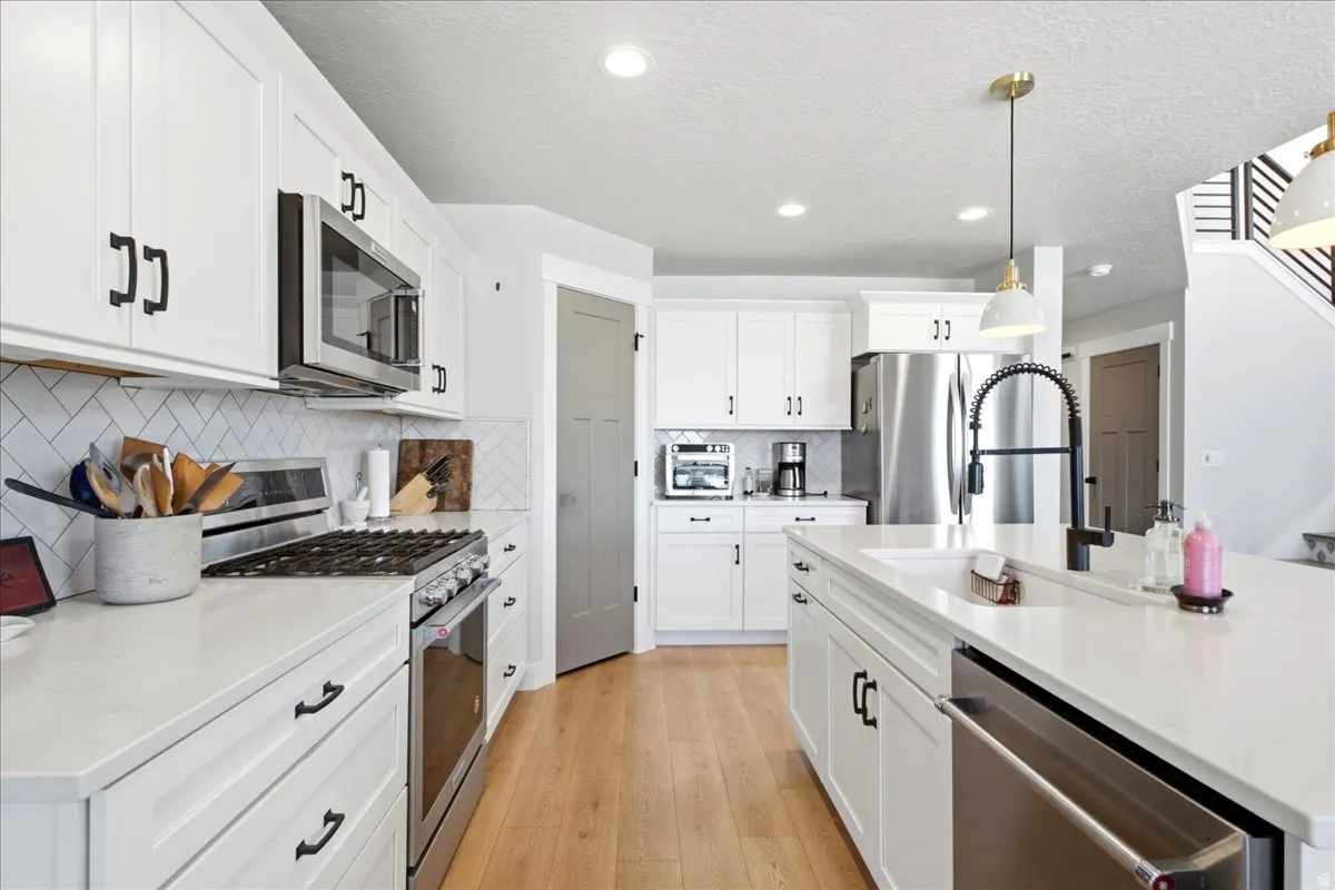 Kitchen featuring white shaker cabinetry, stainless steel appliances, a subway tile backsplash, and a large center island with an undermount sink