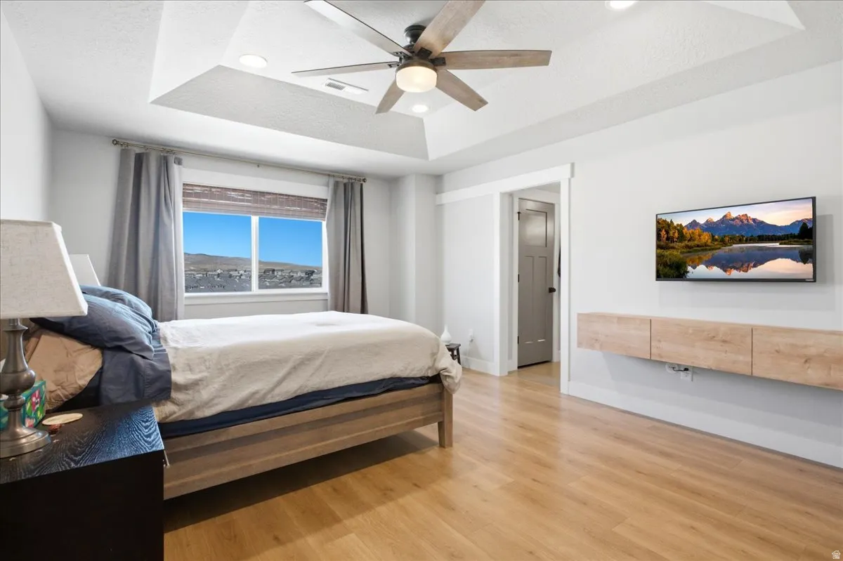 Spacious bedroom featuring light wood-finish flooring and a tray ceiling with recessed lighting