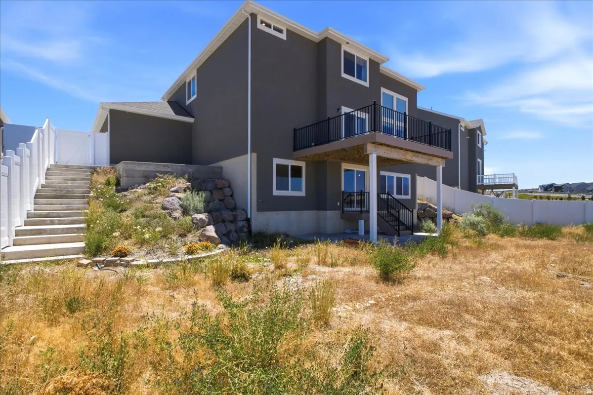 Rear exterior featuring a spacious upper-level balcony with black railing, a lower-level patio, and an external staircase
