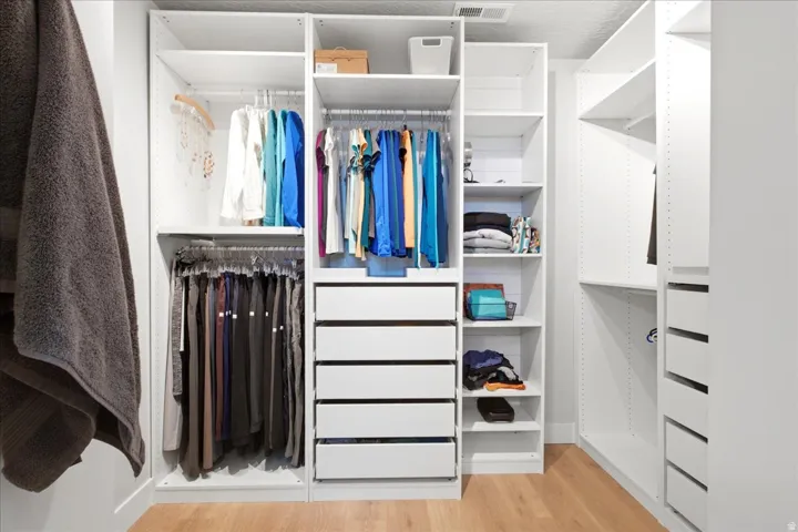 Custom closet system featuring multiple hanging rods, built-in shelving, integrated drawers, and wood-finish flooring
