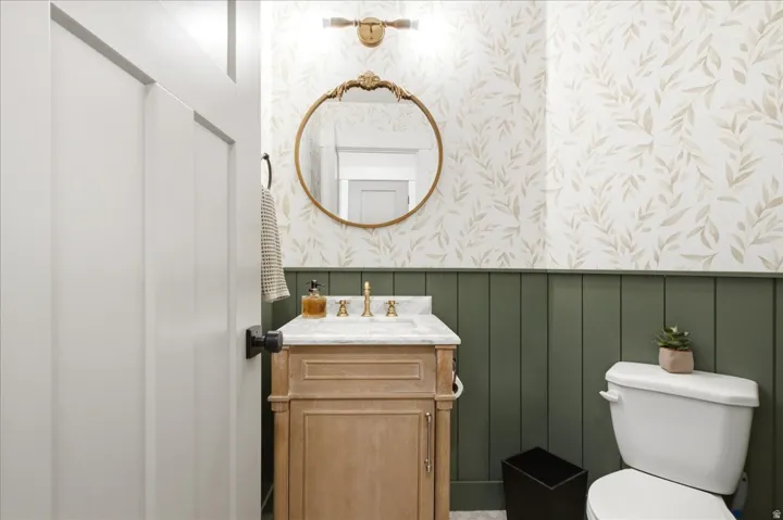 Bathroom featuring a natural wood-finish vanity with a light-colored countertop, a round decorative mirror, and a brass-tone wall sconce