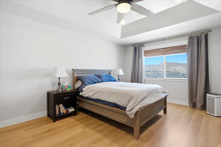 Recessed tray ceiling with ceiling fan, expansive window with mountain scenery, wood-finish flooring, and crisp white walls