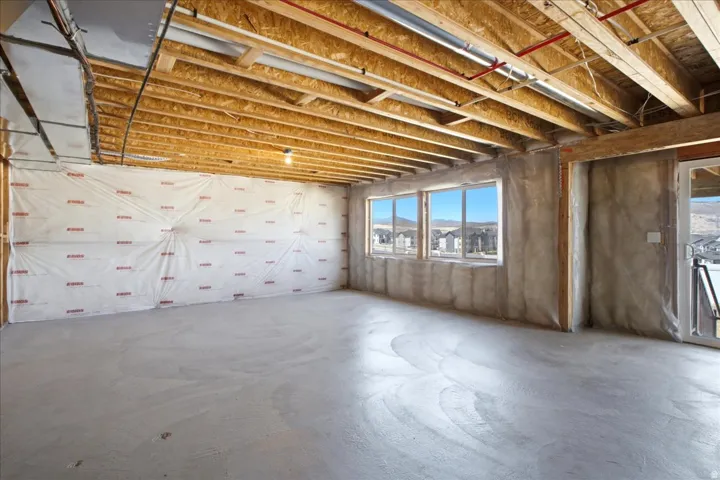 Unfinished basement with concrete flooring, exposed wood joists, and multiple windows