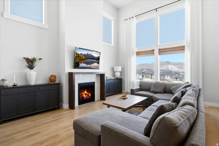 Two-story living area featuring expansive windows with mountain and neighborhood scenery, light wood-finish flooring, and a fireplace with a white tile surround and dark wood mantel