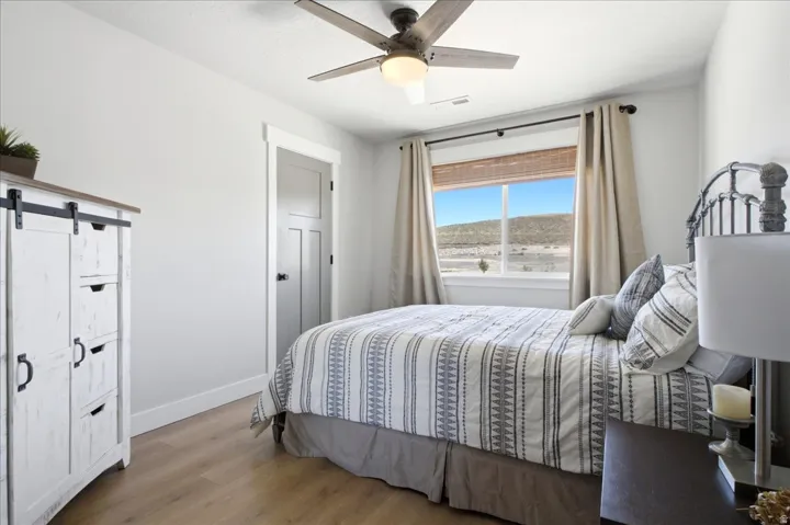 Light-filled interior featuring wood-finish flooring, a ceiling fan with integrated lighting, a multi-pane window with a natural landscape backdrop, and a three-panel interior door with dark hardware