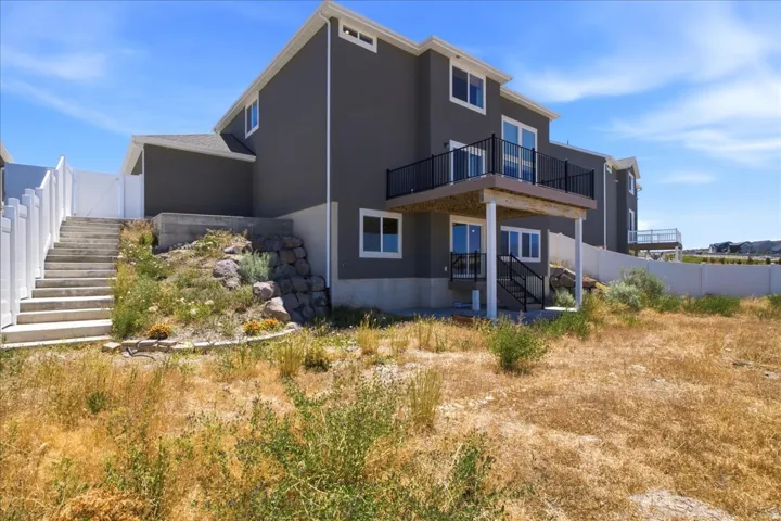Rear exterior featuring a spacious upper-level balcony with black railing, a lower-level patio, and an external staircase