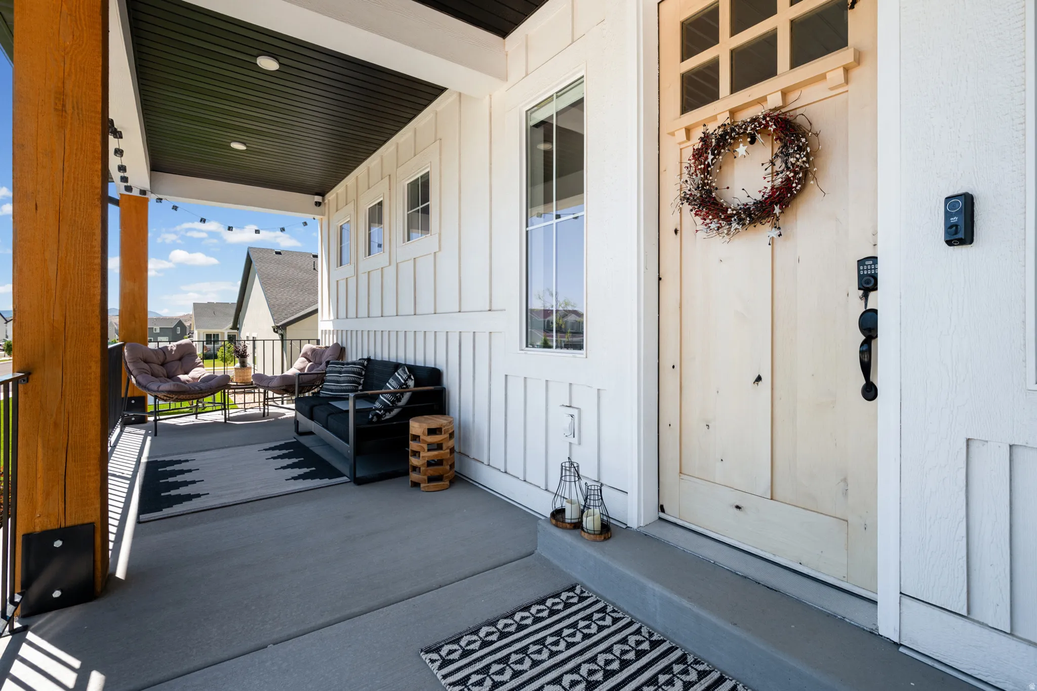 Inviting covered porch featuring a natural wood-finish door with glass inserts, vertical board and batten siding, substantial wood-finish columns, and recessed lighting