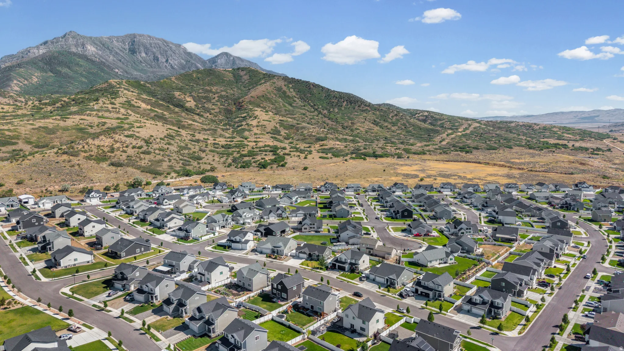 Expansive residential development featuring numerous single-family homes with gray and white exteriors, dark shingle roofs, and green lawns