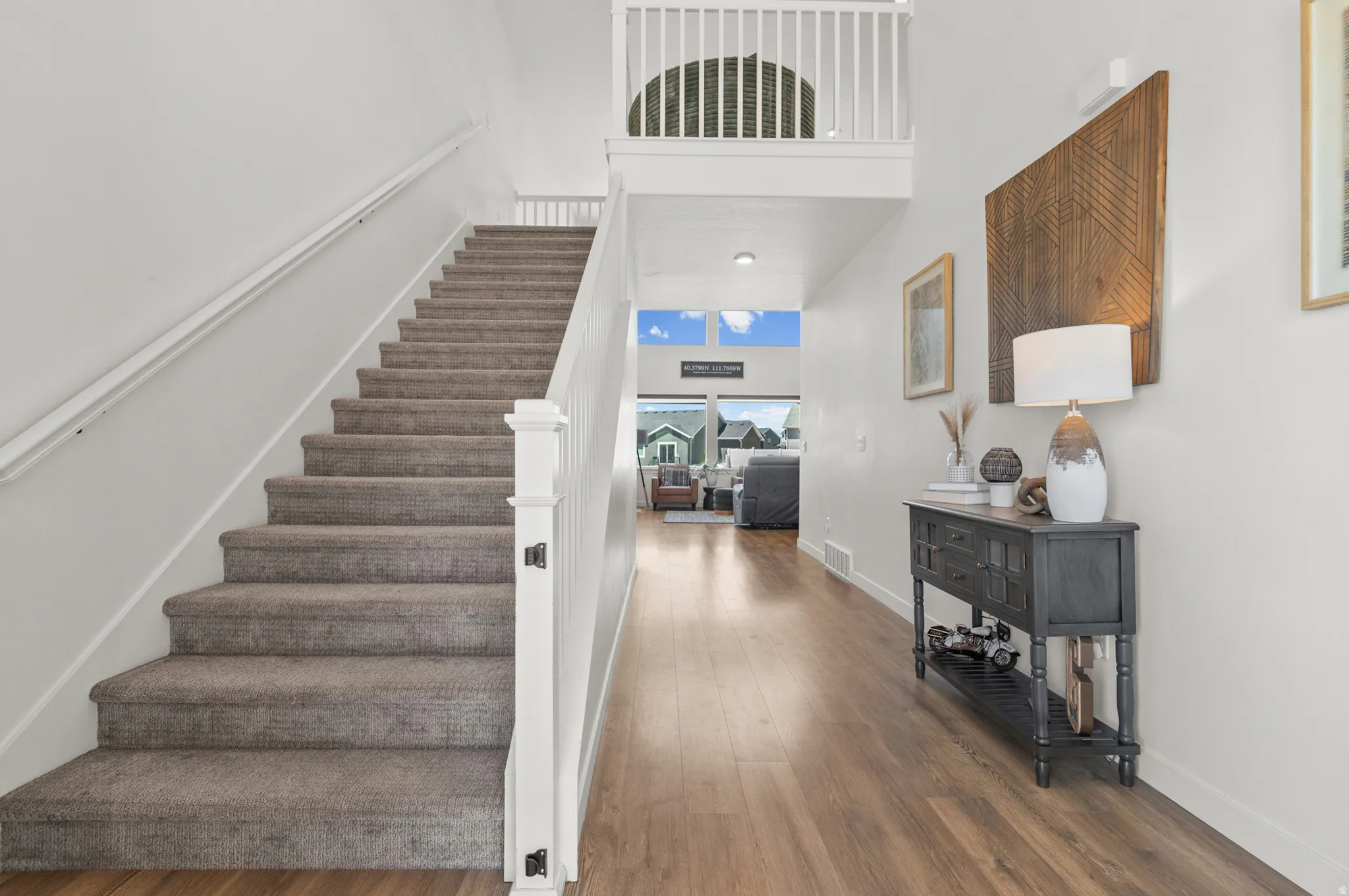 Foyer featuring wood-finish flooring, a carpeted staircase with white balusters, and a second-story landing with an open railing