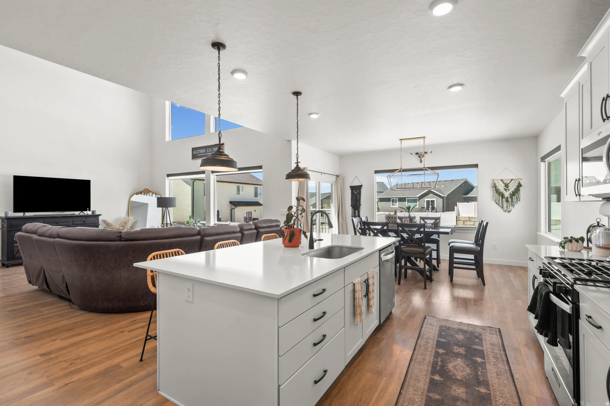 Open-concept living space featuring high ceilings, wood-finish flooring, a kitchen island with a white countertop, and stainless steel appliances