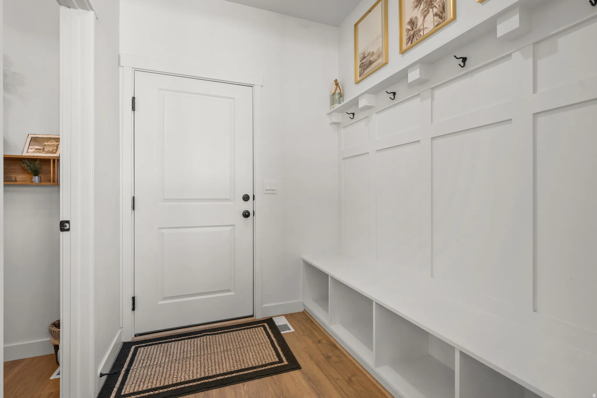 Entryway with wood-finish flooring, featuring a built-in bench, integrated storage cubbies, wall paneling with hooks, and a solid white door