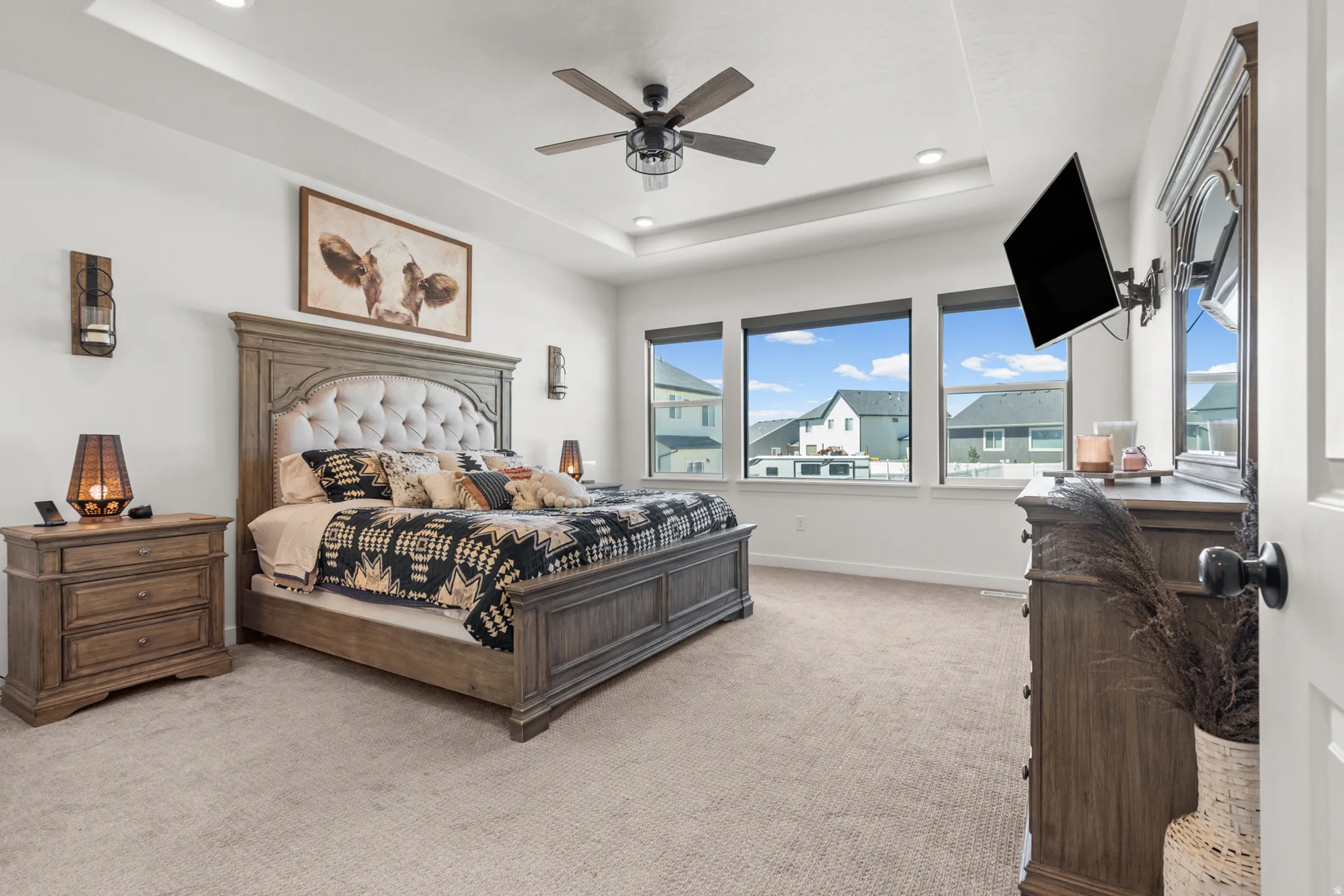 Carpeted bedroom featuring a tray ceiling with recessed lighting and a ceiling fan