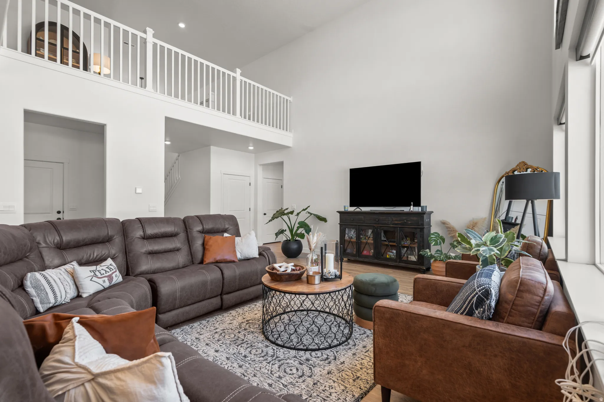 Two-story living area featuring a vaulted ceiling, an upper-level railing, light wood-finish flooring, and a large window