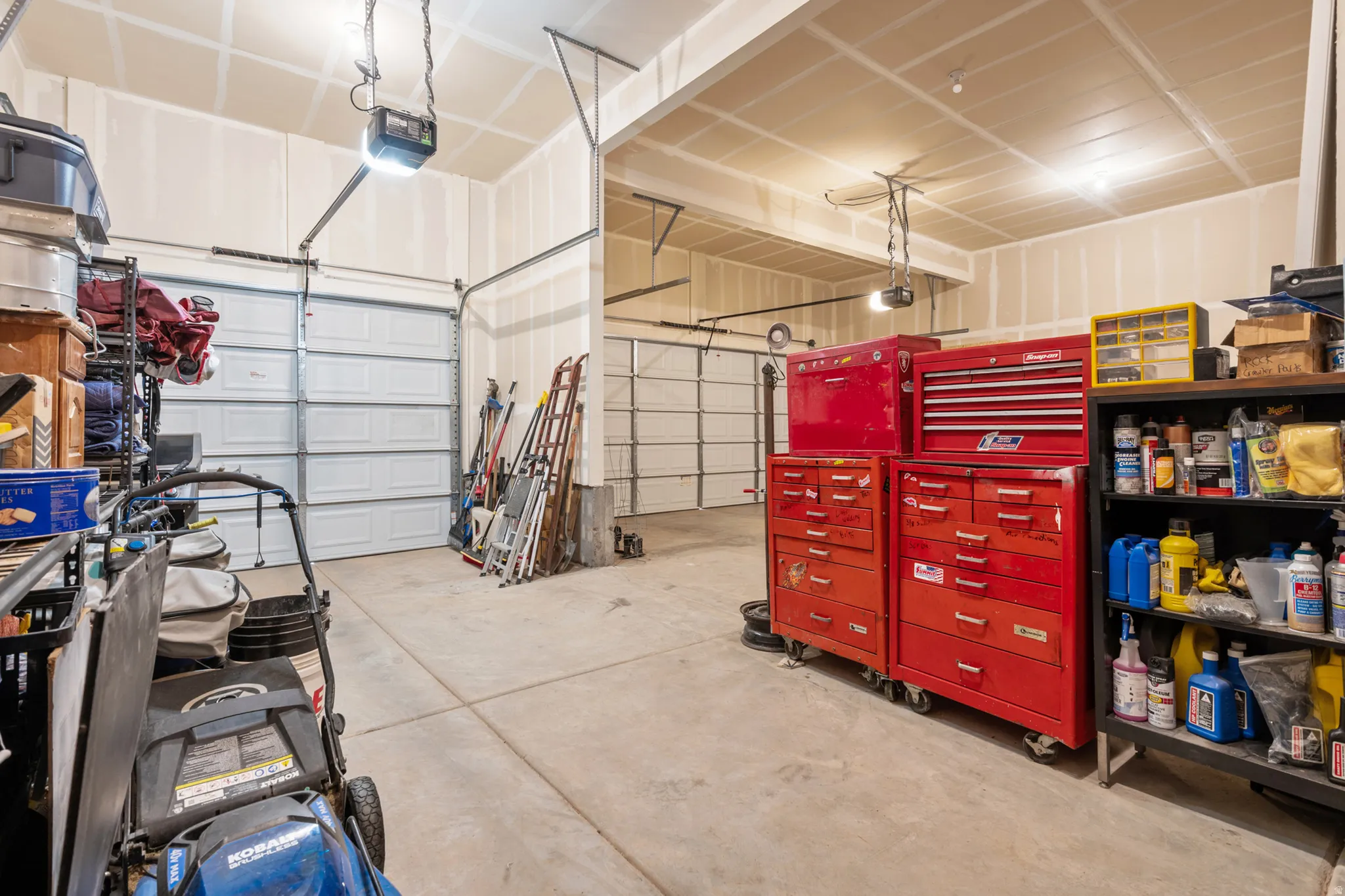 Spacious garage featuring three overhead doors, concrete flooring, exposed ceiling joists, and a built-in shelf unit