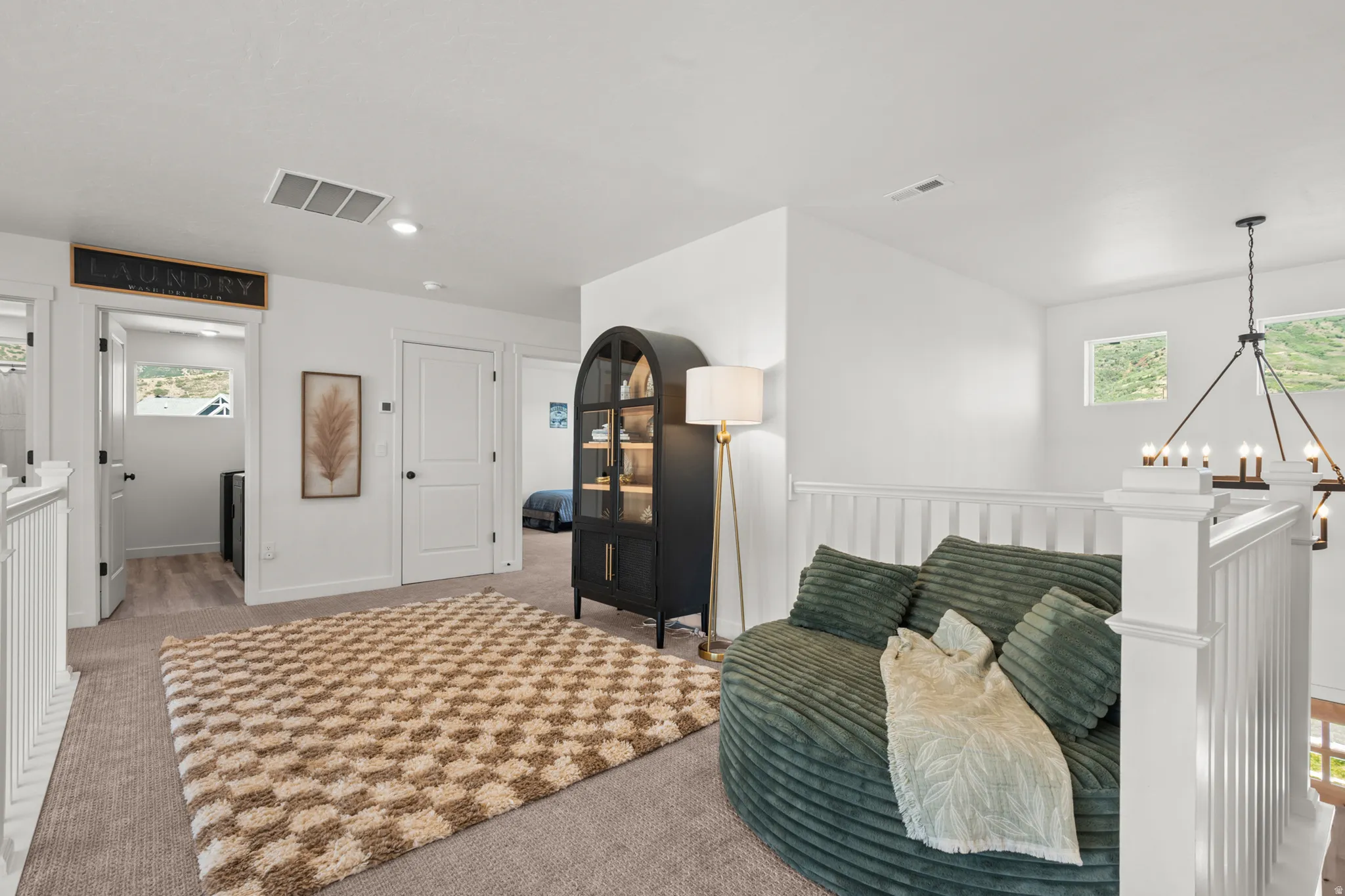 Carpeted landing area featuring white walls, white paneled railing, and a modern chandelier light fixture