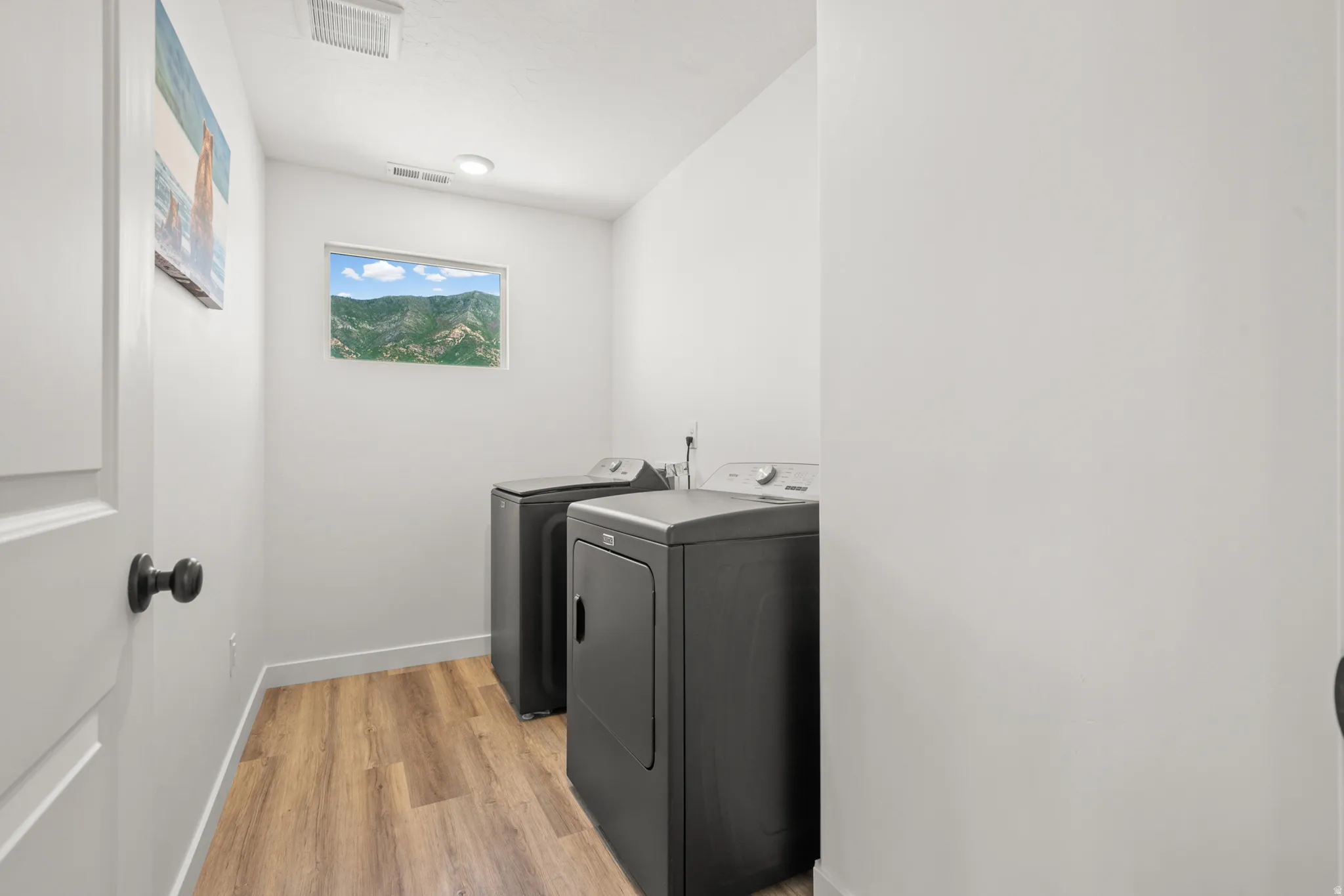 Dedicated utility space featuring wood-finish flooring, a rectangular window, recessed lighting, and a white interior door with matte black hardware