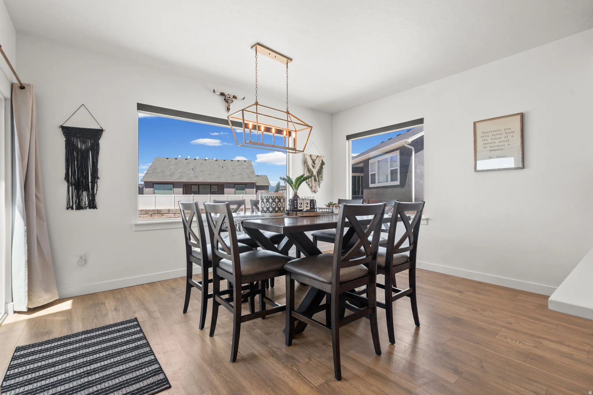 Spacious dining area featuring wood-finish flooring, ample natural light from multiple windows, and a contemporary linear chandelier