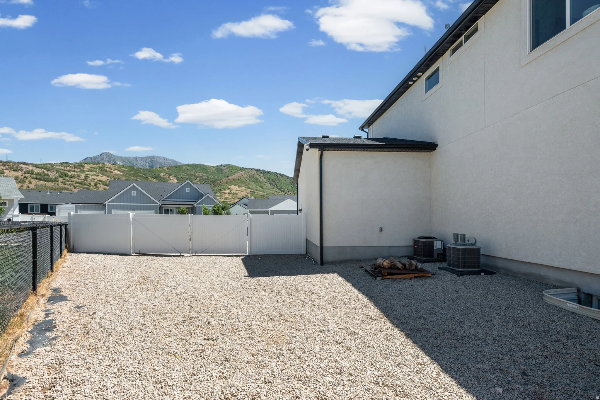 Expansive gravel side yard with partial chain link fencing and a white privacy fence