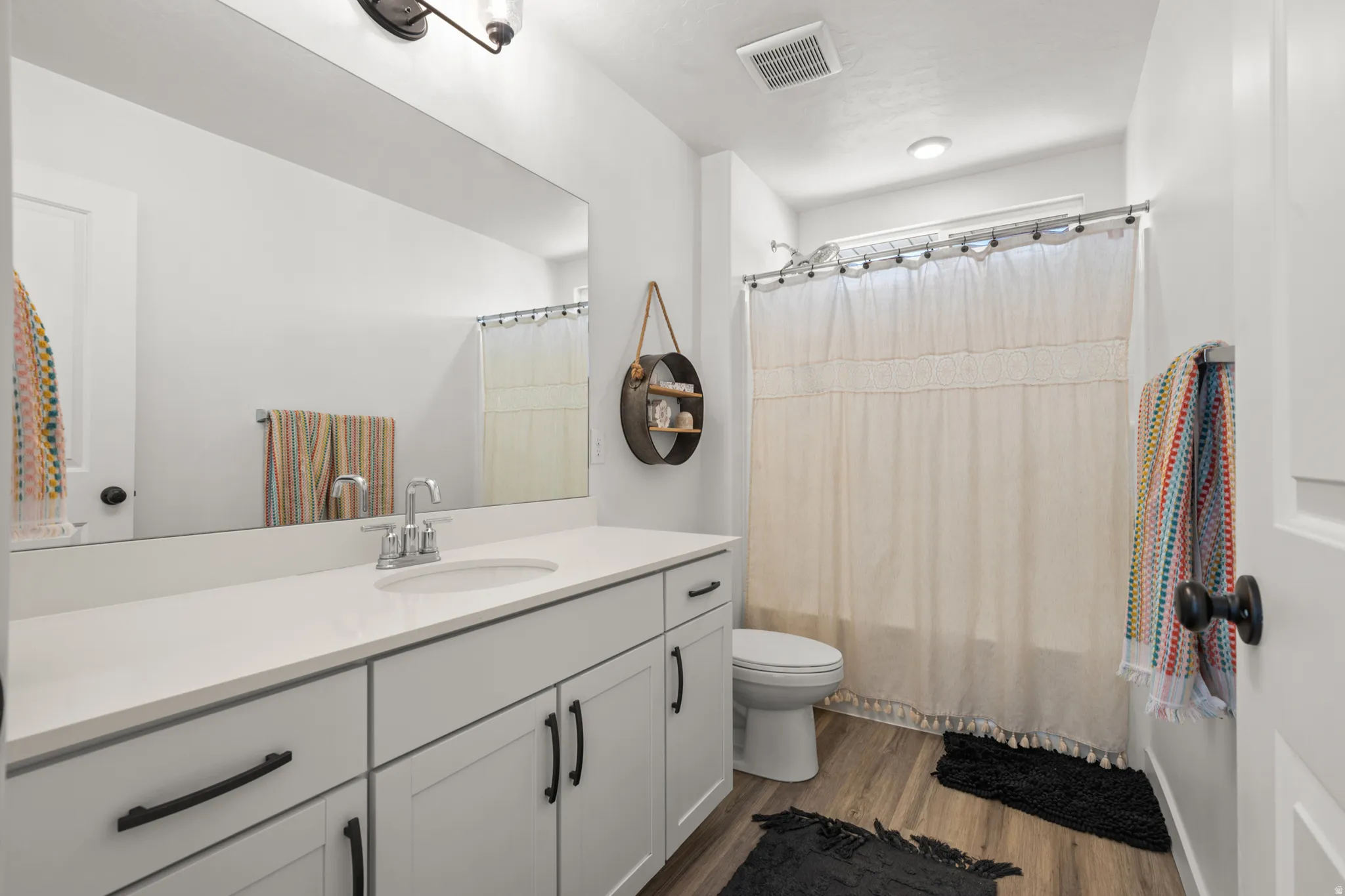 Bathroom featuring a white vanity with matte black hardware, a large mirror, a chrome faucet, light wood-finish flooring, and a white toilet