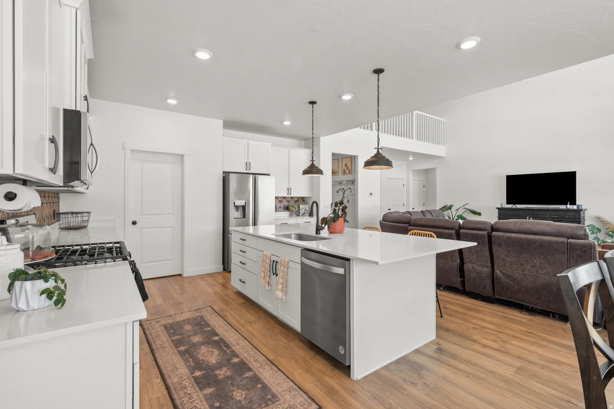 Open-concept kitchen featuring an oversized island with seating, stainless steel appliances, white cabinetry, quartz countertops, and wood-finish flooring