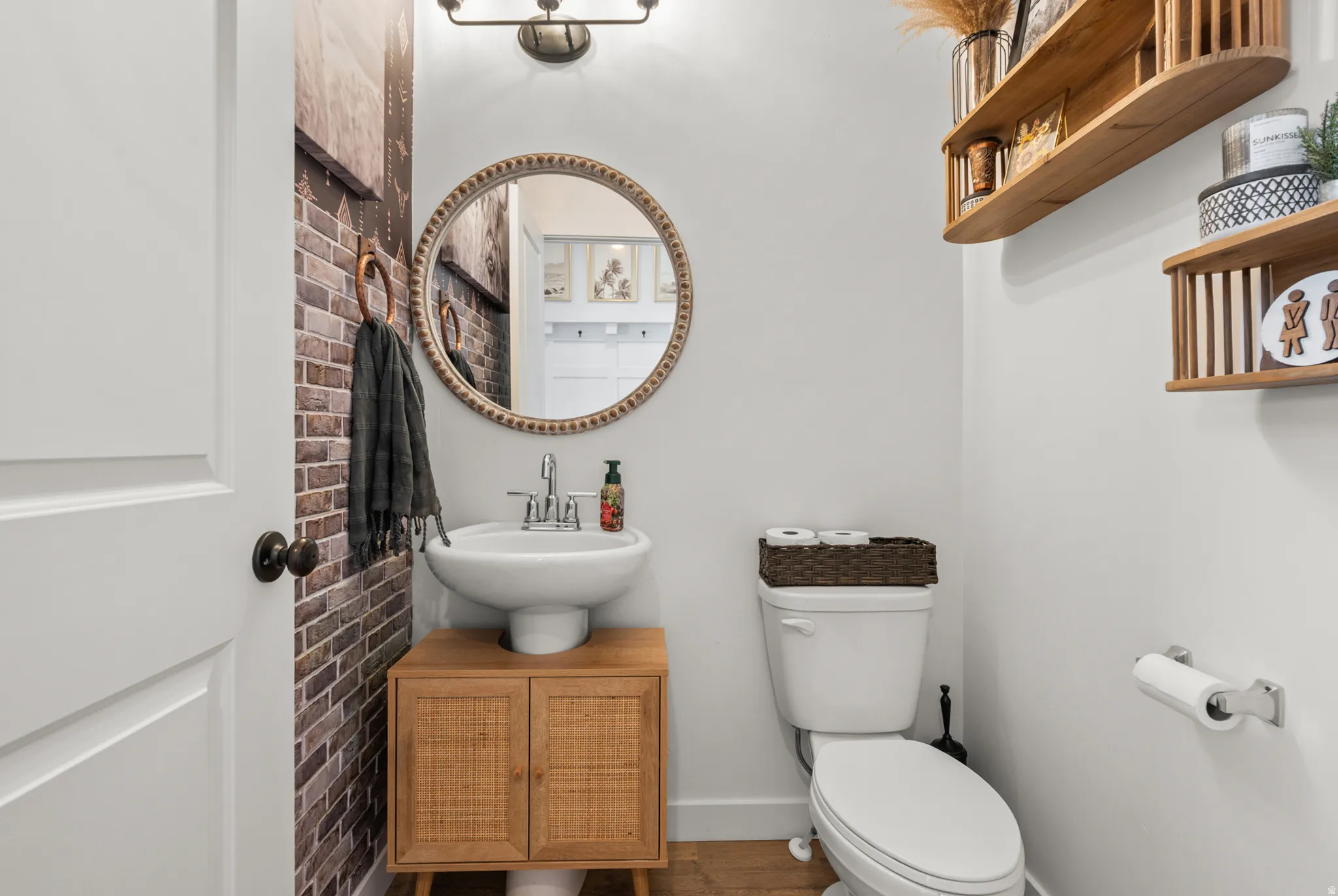 Powder room featuring a pedestal sink with a wood-finish vanity, a decorative circular mirror, and a wall-mounted light fixture