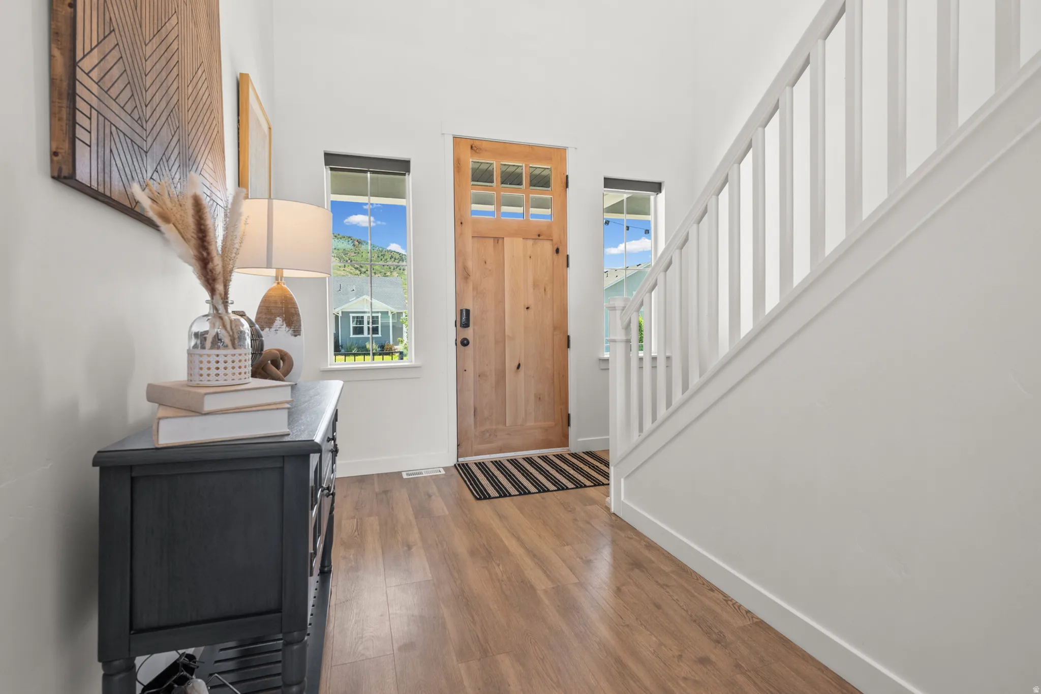 Entryway featuring a natural wood-finish door with glass panels, wood-finish flooring, white painted walls, and a staircase with white spindles