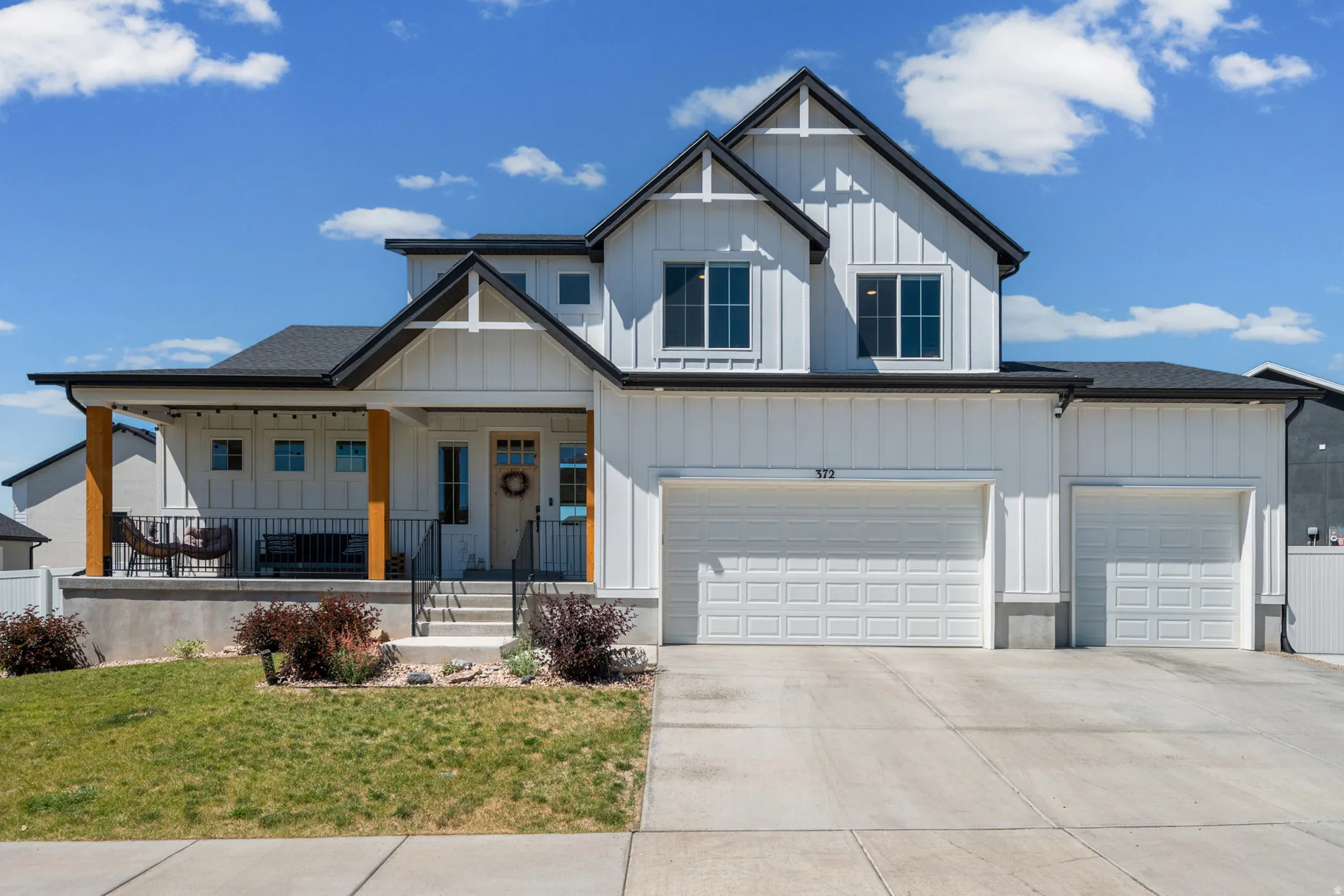 Contemporary farmhouse-style exterior featuring white board and batten siding, dark trim, a covered porch with natural wood pillars, a three-car garage, and a concrete driveway