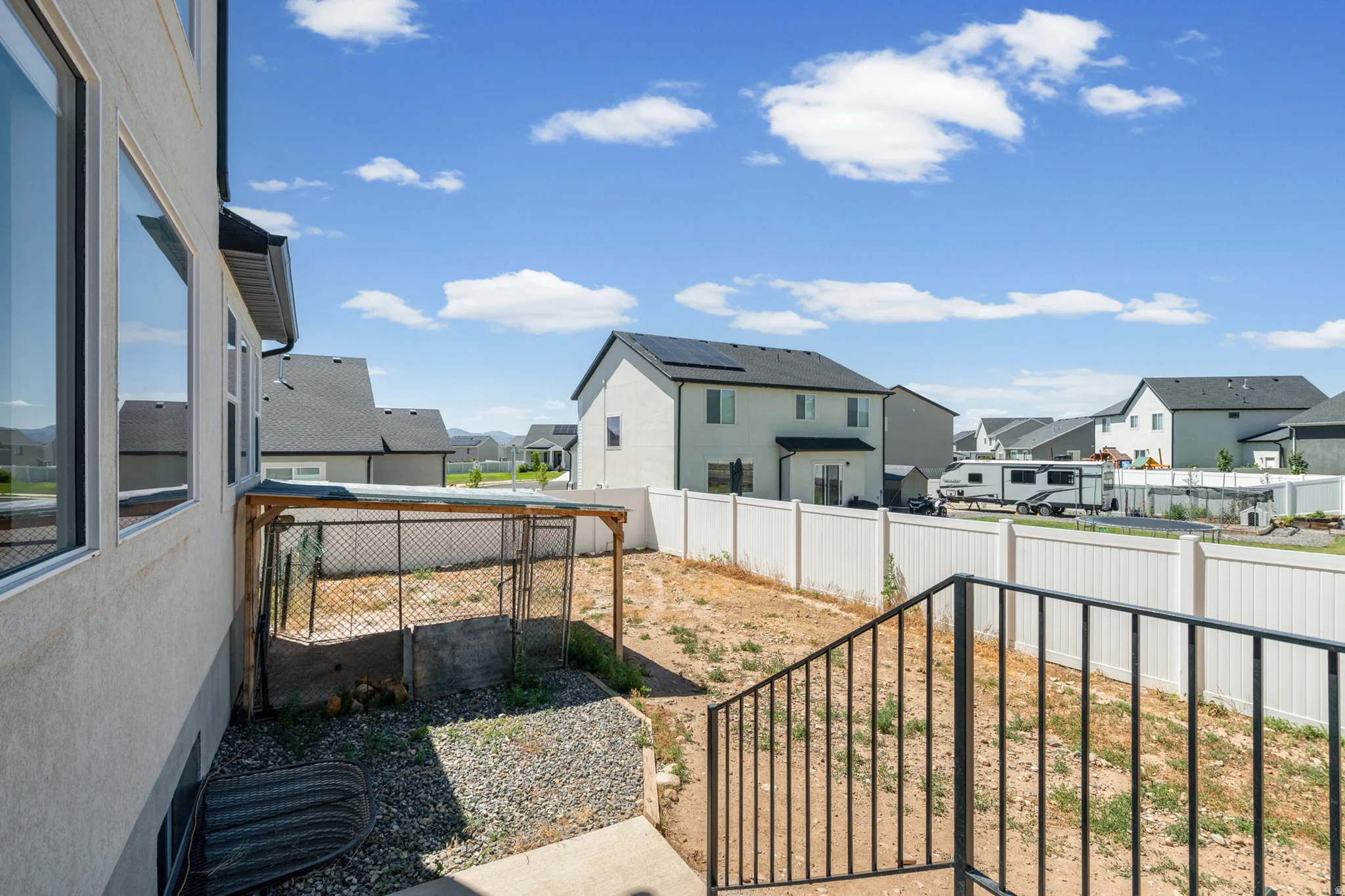 Rear exterior featuring a concrete patio with black metal railings, a white privacy fence, and a chain-link enclosure