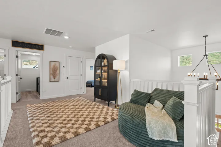 Carpeted landing area featuring white walls, white paneled railing, and a modern chandelier light fixture