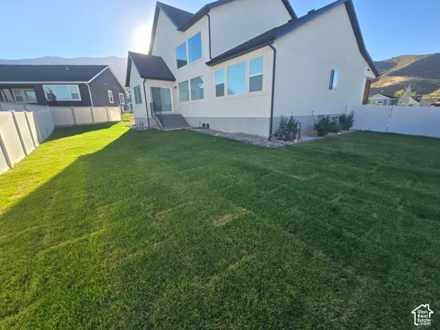 Expansive lawn area, white stucco exterior, black-framed windows, rear sliding glass door, and mountain scenery