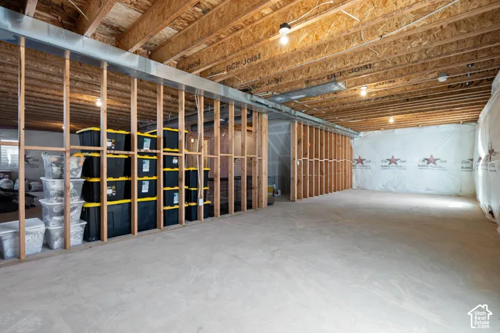 Unfinished basement featuring exposed wood joists, concrete flooring, and framed walls