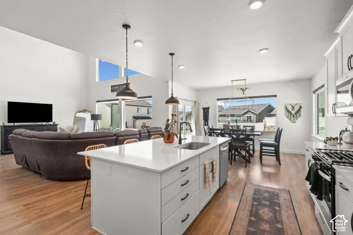 Open-concept living space featuring high ceilings, wood-finish flooring, a kitchen island with a white countertop, and stainless steel appliances