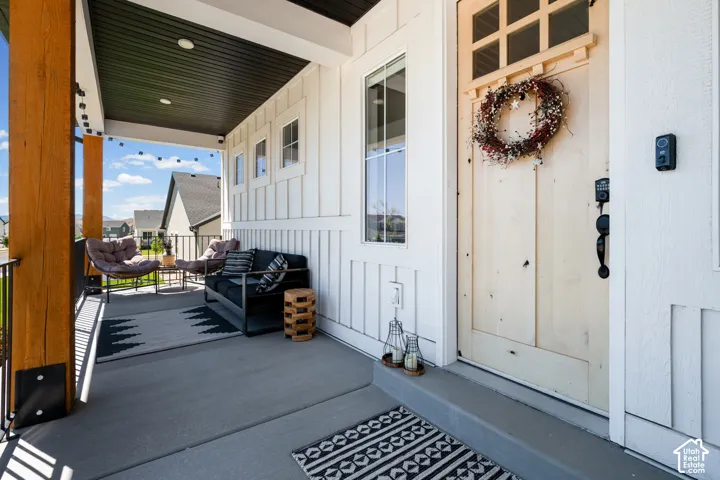 Inviting covered porch featuring a natural wood-finish door with glass inserts, vertical board and batten siding, substantial wood-finish columns, and recessed lighting