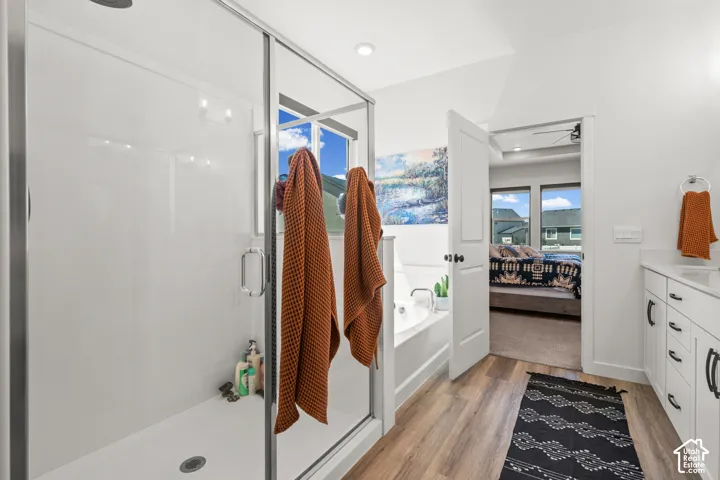 Glass-enclosed shower with a built-in bench, a soaking tub, wood-finish flooring, a white vanity with a white countertop, and dark-finish hardware