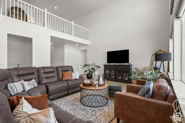 Two-story living area featuring a vaulted ceiling, an upper-level railing, light wood-finish flooring, and a large window