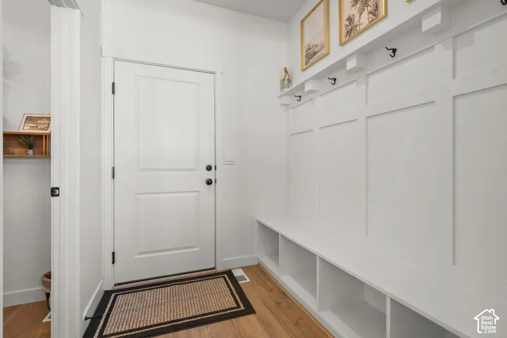 Entryway with wood-finish flooring, featuring a built-in bench, integrated storage cubbies, wall paneling with hooks, and a solid white door