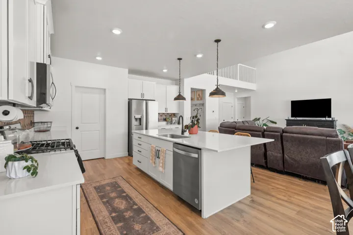 Open-concept kitchen featuring an oversized island with seating, stainless steel appliances, white cabinetry, quartz countertops, and wood-finish flooring