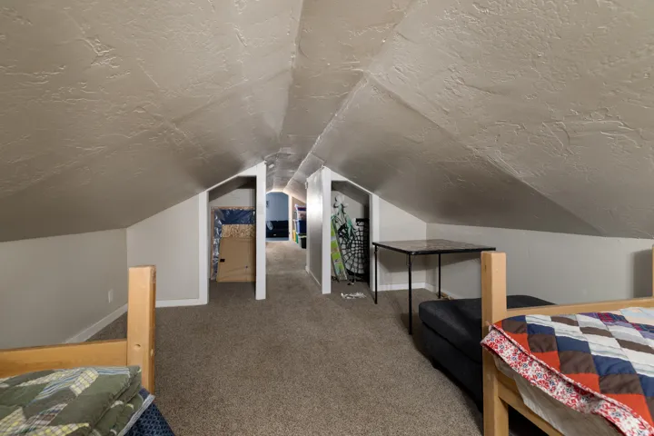 Attic space featuring sloped ceilings, textured walls, and light-toned carpeting