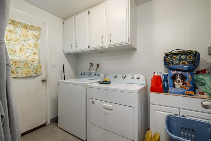 Dedicated laundry area featuring a washer and dryer, upper white cabinetry, and a lower built-in cabinet with countertop space