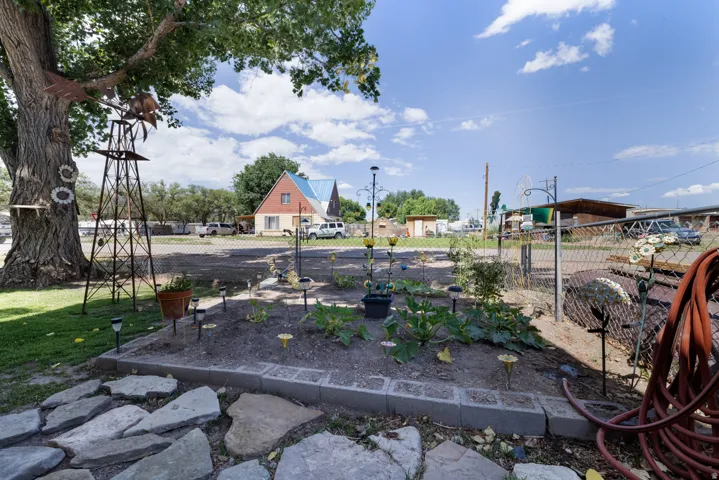 Established garden area with a stone paver path, raised beds, and mature tree shading a portion of the yard