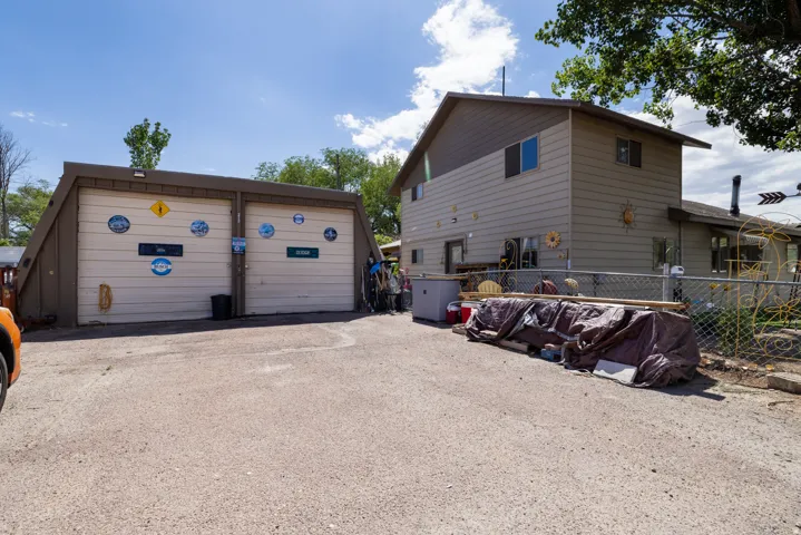 Two-car garage with angled brown siding, gravel driveway, and a two-story residence with beige siding