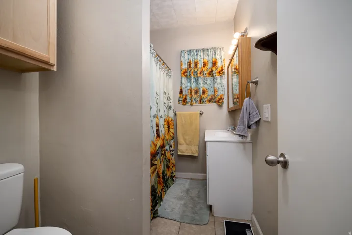 Bathroom featuring a white vanity with a porcelain sink, tiled flooring, wood-finish medicine cabinet, and sconce lighting