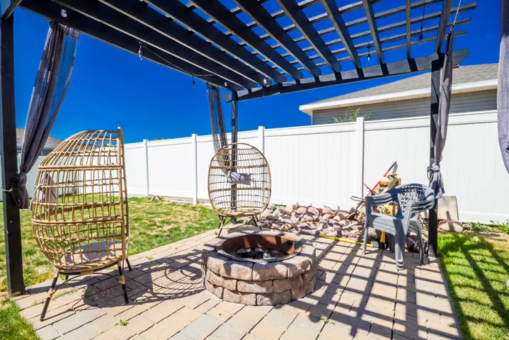 Outdoor patio featuring a stone-clad fire pit, paver flooring, and a dark-stained wood pergola with string lighting