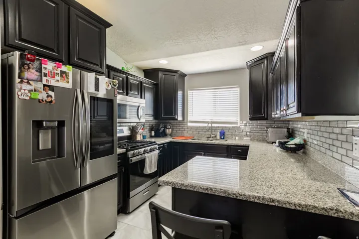 Kitchen featuring dark cabinetry, stainless steel appliances, granite countertops, and a white subway tile backsplash