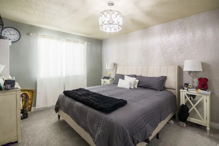 Plush carpeted bedroom featuring an upholstered headboard, a textured accent wall, and a crystal chandelier