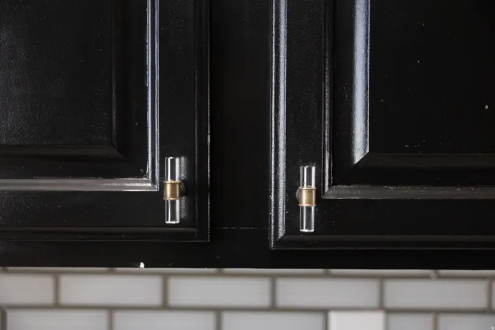 Black cabinetry with clear cylindrical pulls featuring brass accents, set above a white subway tile backsplash